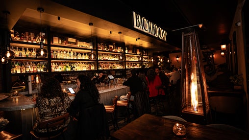 Interior del bar Backroom con estanterías iluminadas repletas de botellas, clientes conversando en la barra y un ambiente acogedor con luces cálidas.