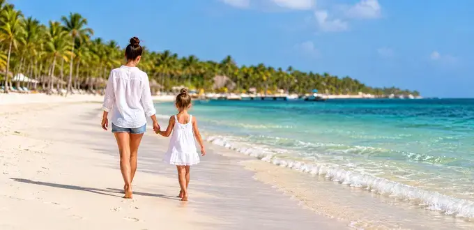 Madre e hija caminando por una playa de Punta Cana, República Dominicana, junto al mar turquesa y palmeras tropicales.