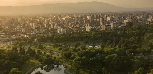 Vista panorámica de San Miguel de Tucumán, Argentina, con parques, edificios y sierras al fondo.