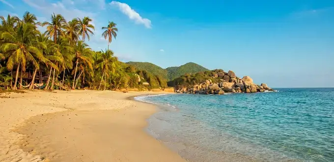 Playa tropical en el Parque Tayrona, Santa Marta, Colombia, con palmeras, mar Caribe y formaciones rocosas.