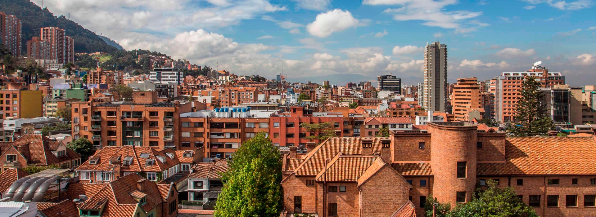 Vista panorámica de Bogotá con edificios de ladrillo y cerros al fondo bajo un cielo parcialmente nublado.