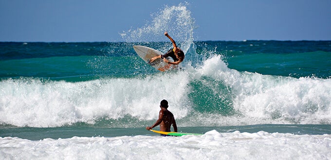 Surfista realizando una maniobra sobre una ola en Pipa, Brasil, mientras otro deportista espera en el agua disfrutando del mar.
