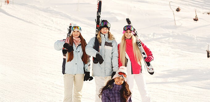 Grupo de amigas con equipo de esquí sonriendo en la nieve, disfrutando una jornada de invierno en la montaña.
