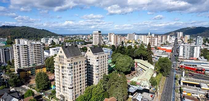 Vista aérea de Temuco con edificios residenciales, áreas verdes, avenidas principales y cerros al fondo, Temuco, Chile.