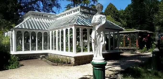 Invernadero histórico con estructura de vidrio y estatua clásica en jardines patrimoniales, Parque Isidora Cousiño, Lota, Chile.