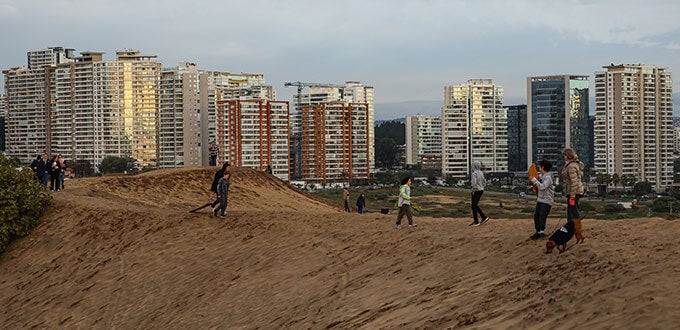 Personas caminando y jugando en las dunas de Concón, con edificios residenciales al fondo, naturaleza urbana, Región de Valparaíso, Chile.
