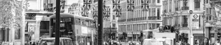 Busy central London street with buses, taxis and Union Jack banners hanging over the street.