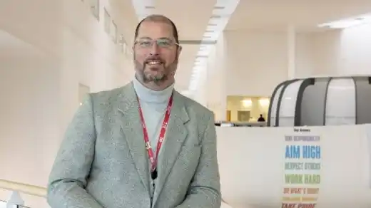 An image of a man wearing glasses and wearing a grey jacket