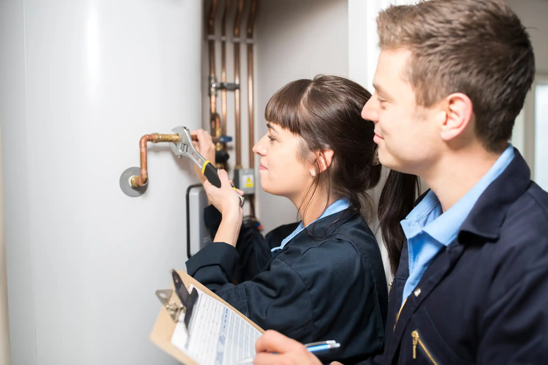 Female Trainee Plumber Working On Central Heating Boiler With Male Engineer