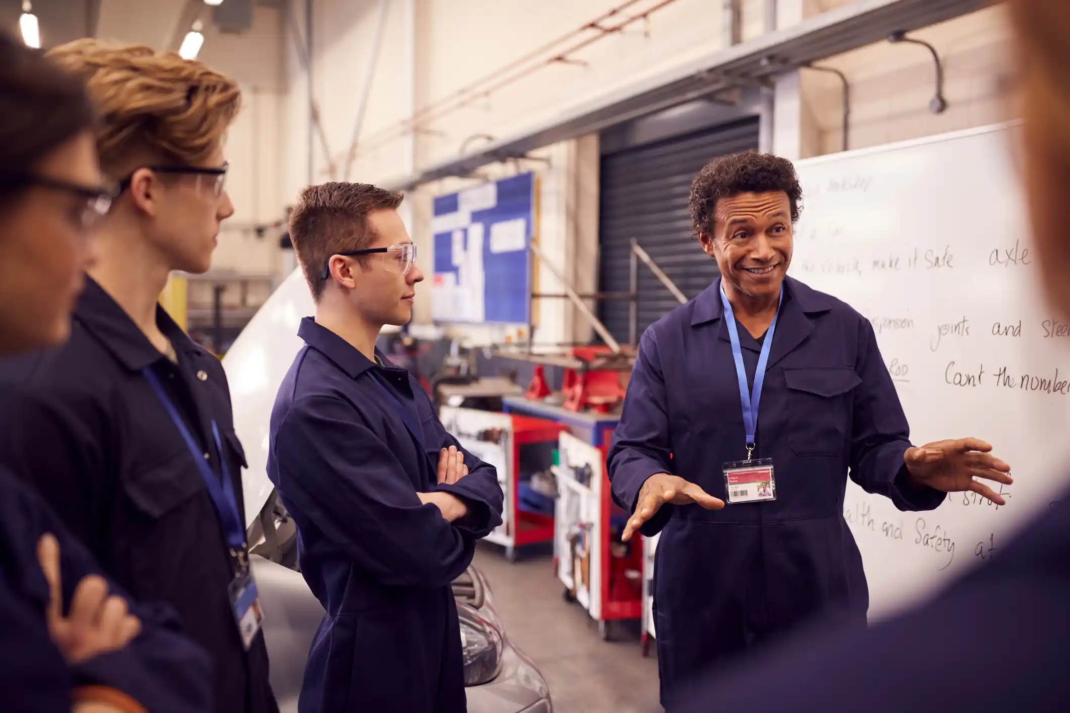 A man is explaining something to students inside an auto repair garage