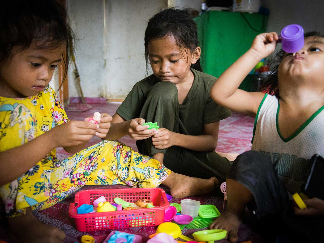 Three young girls seated on the floor playing with a tea set.