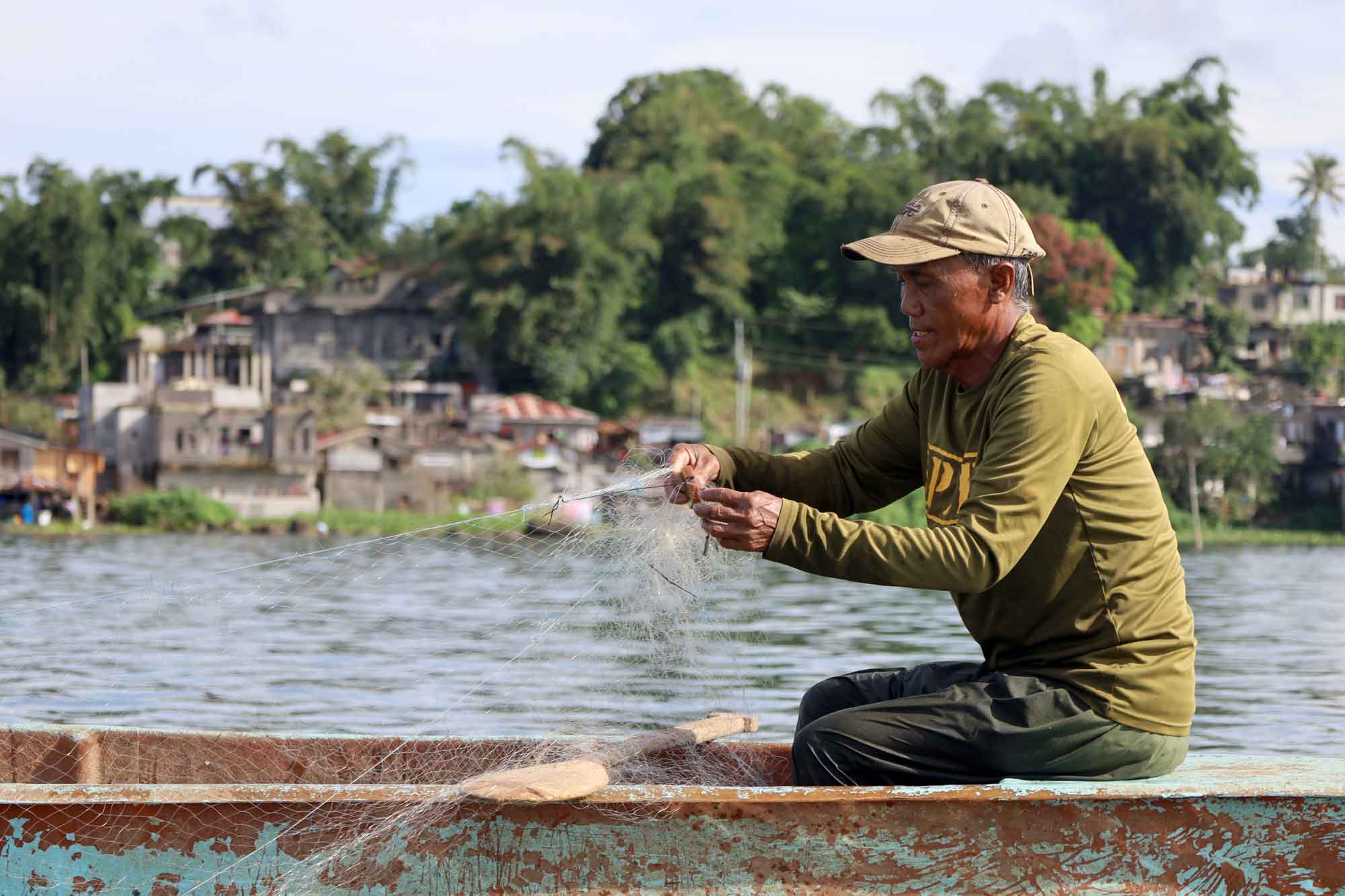 A man is seated in a canoe on a lake, reeling in a fishing line.  