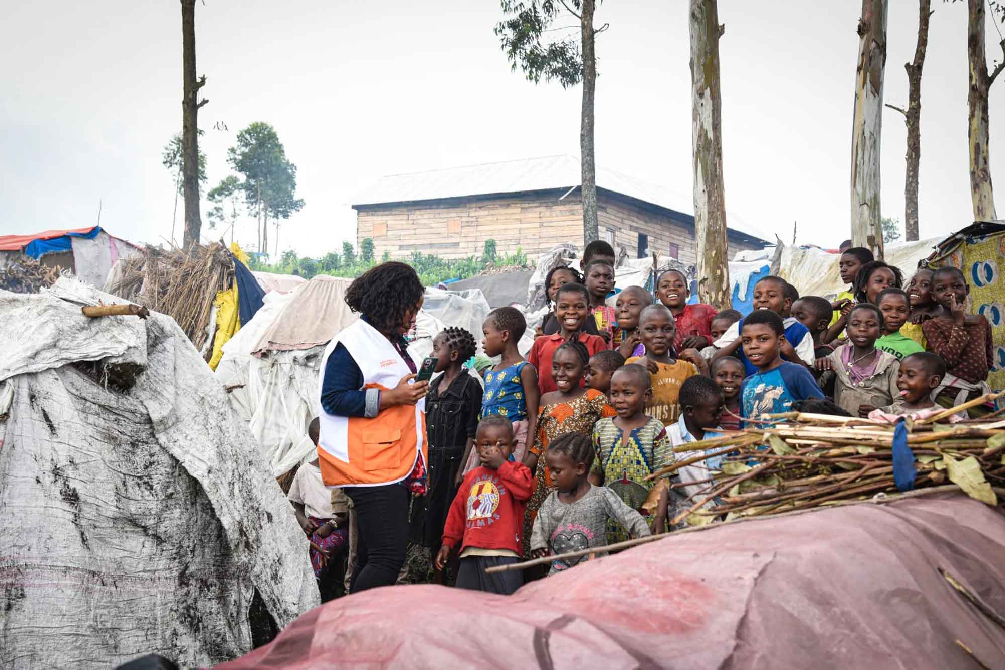 A group of children outside gather around and smile as a World Vision staff speaks to them.