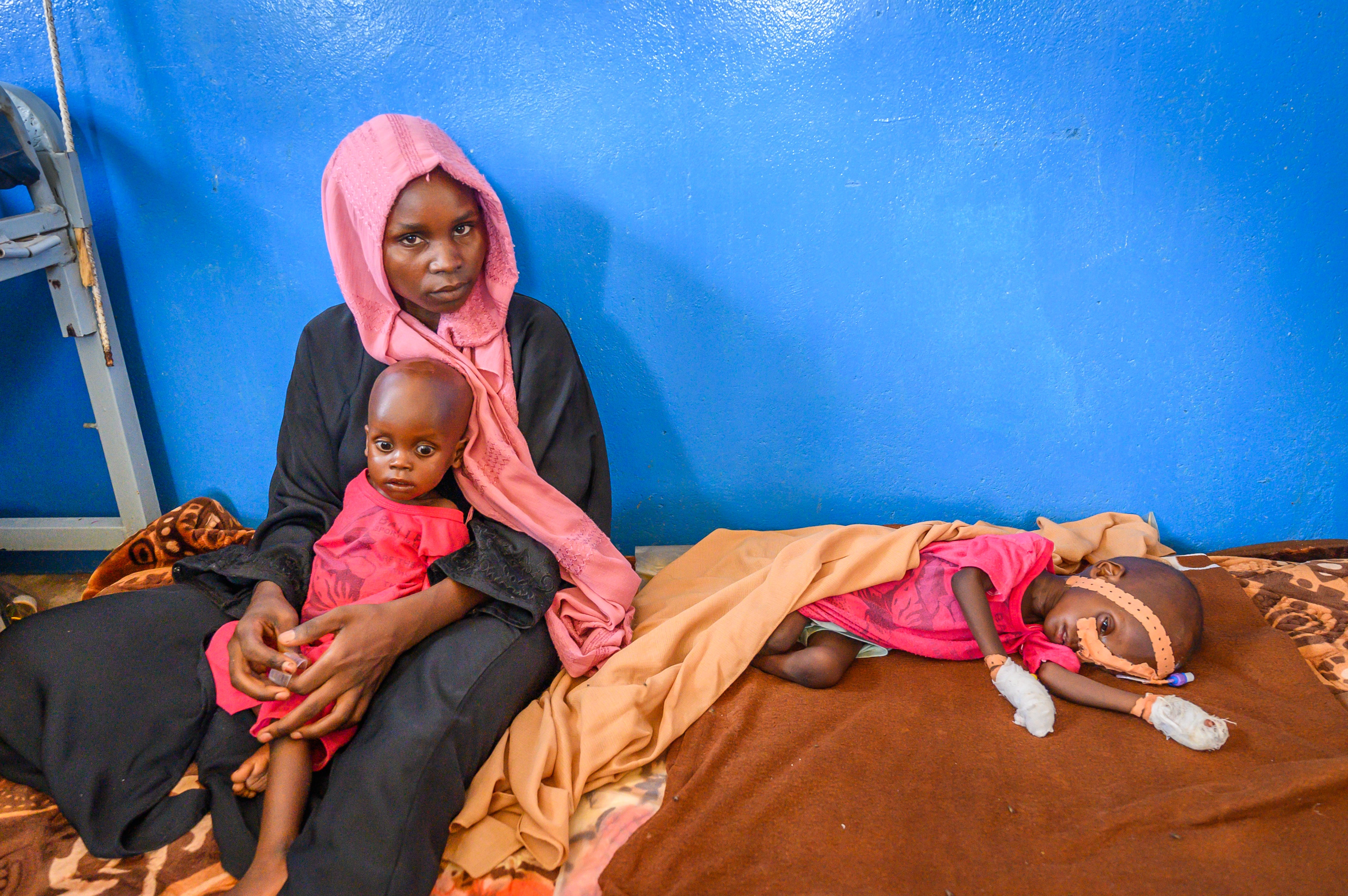 A young Sudanese mother sits in a nutrition clinic with her very ill twin boys