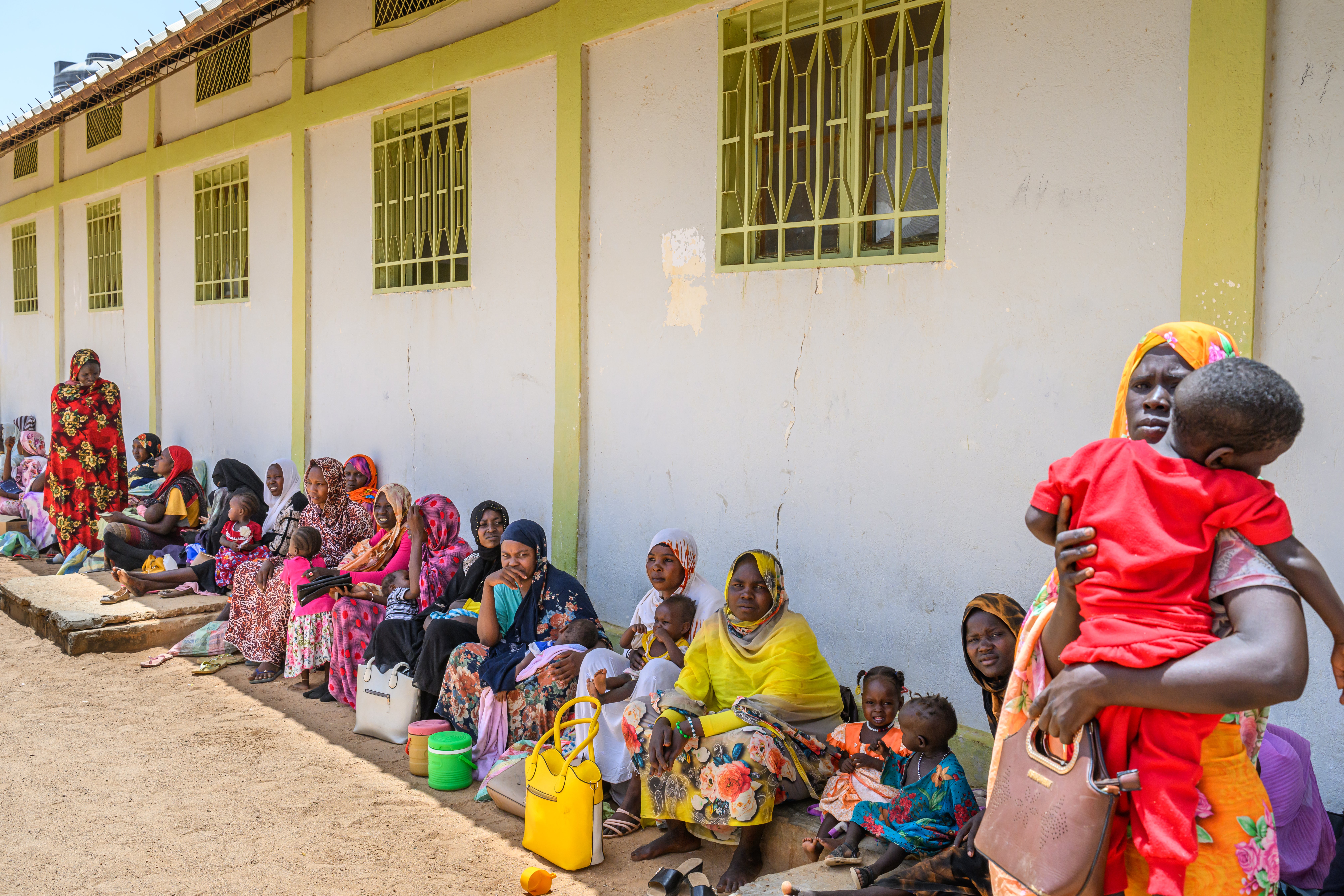 Sudanese refugee women line up outside a nutrition clinic with their children waiting to be seen.