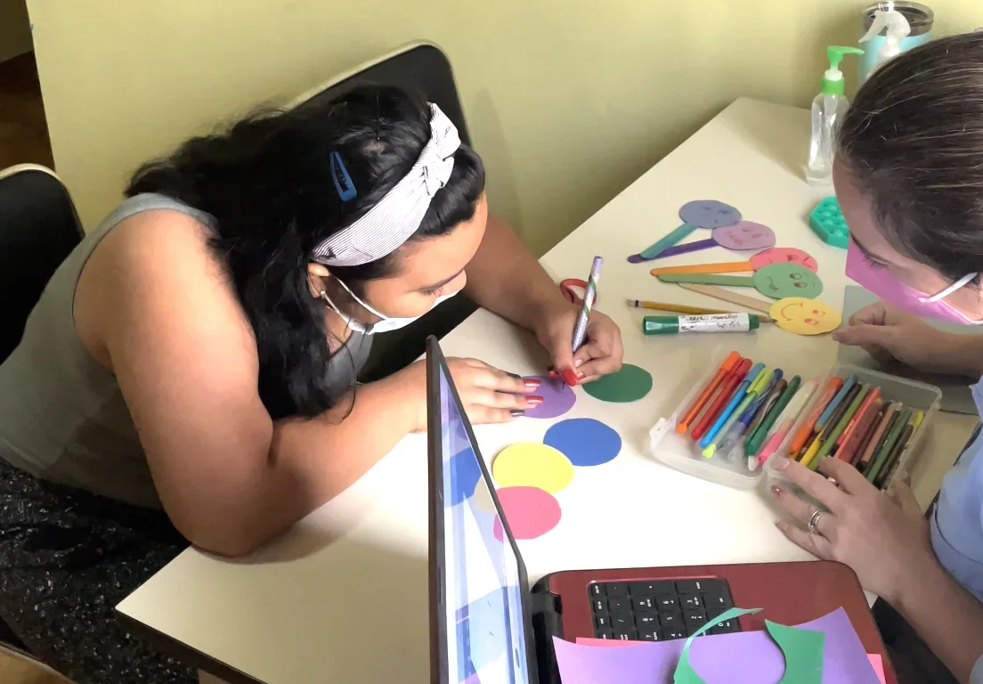 Two girls sitting at a desk, working on an art project together.
