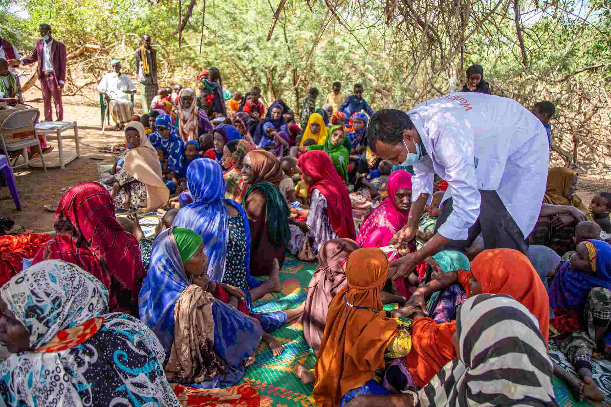 In an Internally Displaced Persons camp in Somalia, a group of people sit on the ground while World Vision staff distribute essential food and supplies. 