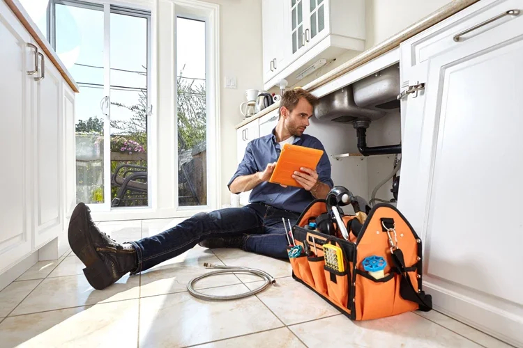 Plumber with tools doing repairs in the kitchen. If a House is Damaged Due to the Builders, Who's Responsible?