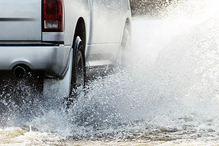 A truck plows through flood waters on a rural road. If My Car was Damaged Due to Flooding, Will Insurance Cover It?