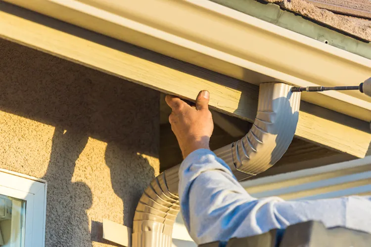 Worker Attaching Aluminum Rain Gutter to Fascia of House. If the Gutters Weren't Installed Right and Your Basement Floods, Who's Responsible?
