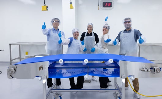 Group of SET participants in white PPE cheering behind a clean conveyor