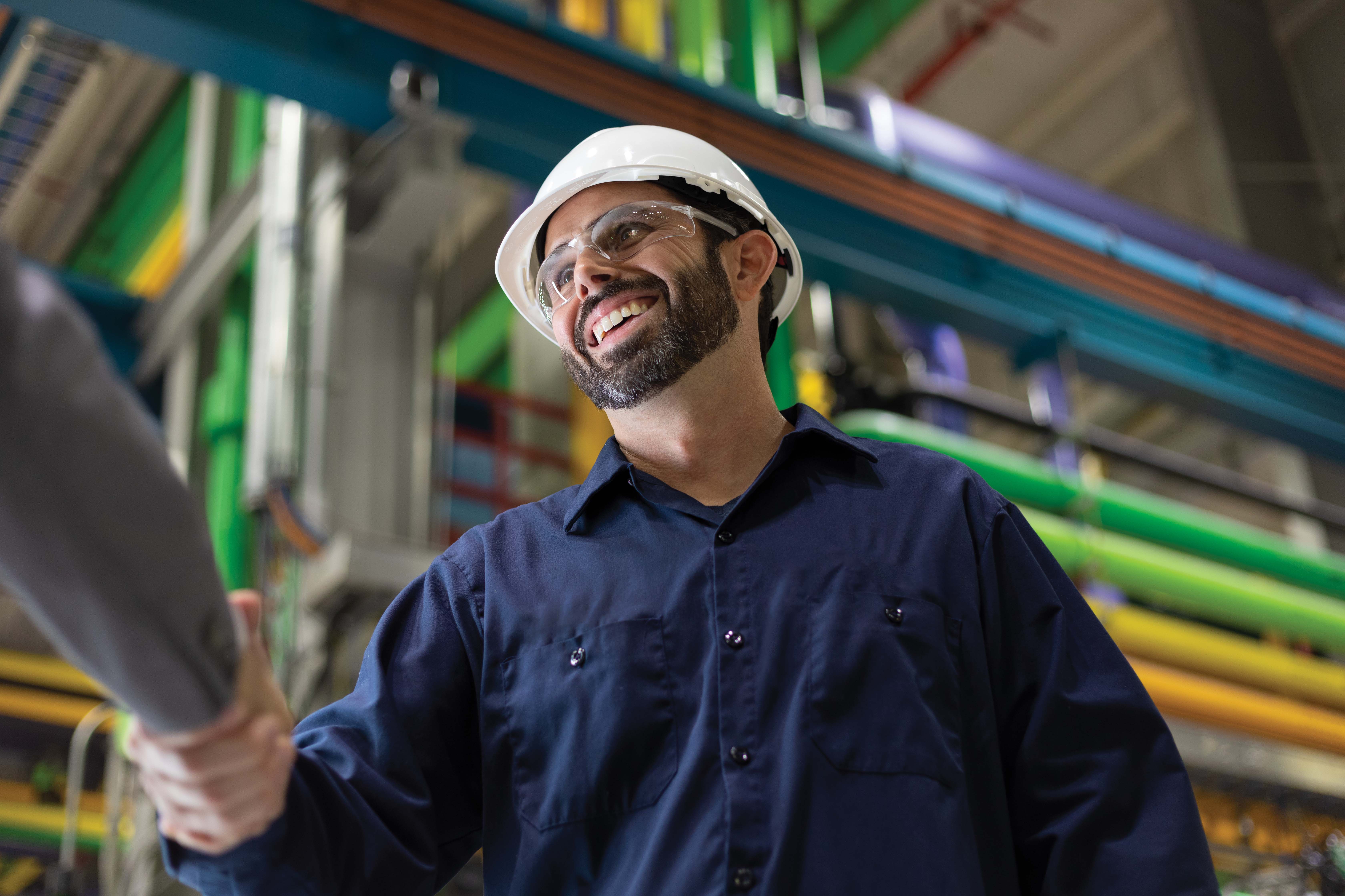 Man, wearing safety helmet and glasses, shaking hands in a plant