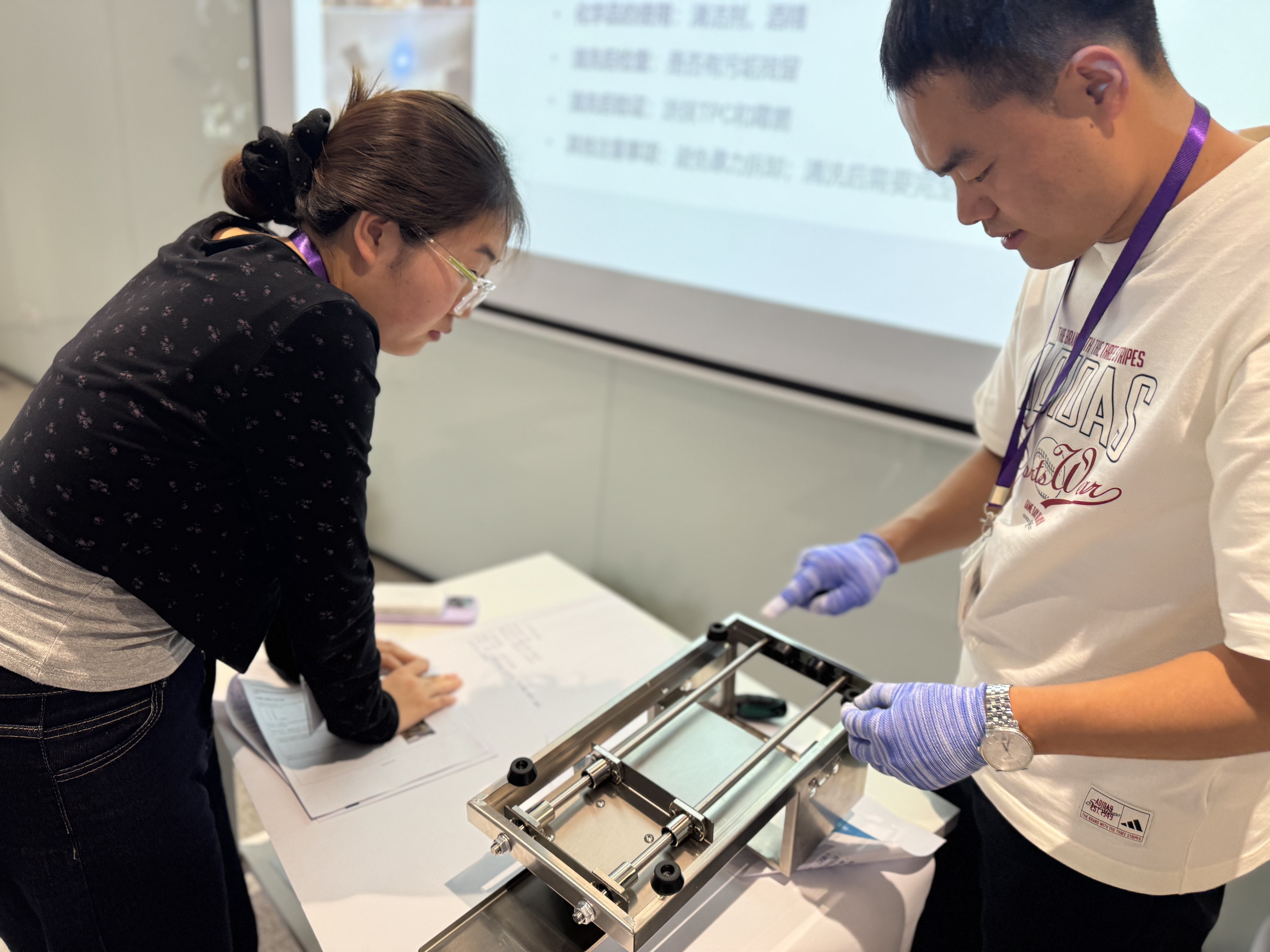 Two participants inspect a small piece of equipment during Yeast and Mold Control Training