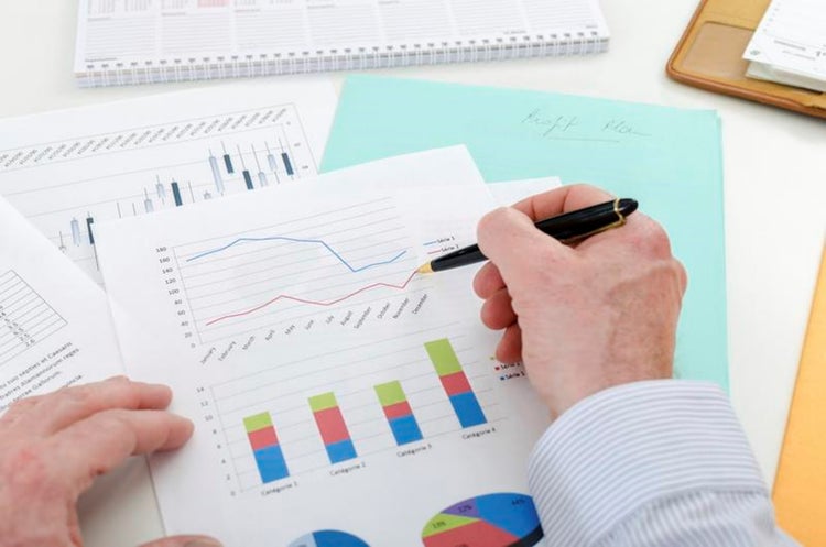 Bar charts, trendlines, pie charts with a hand holding a pen.