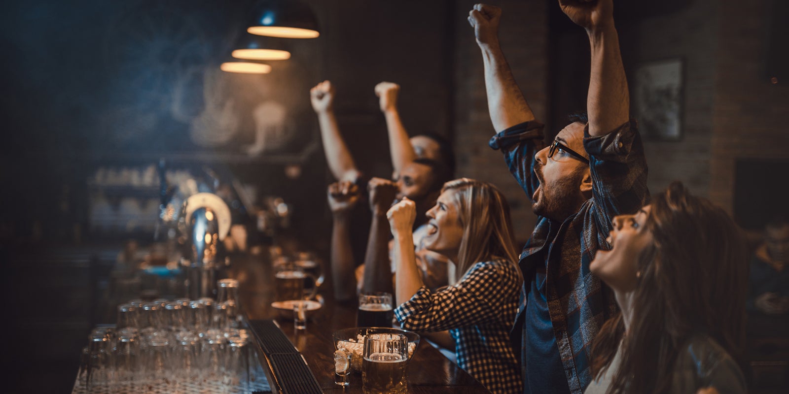 A group of people sitting at a bar with their hands up