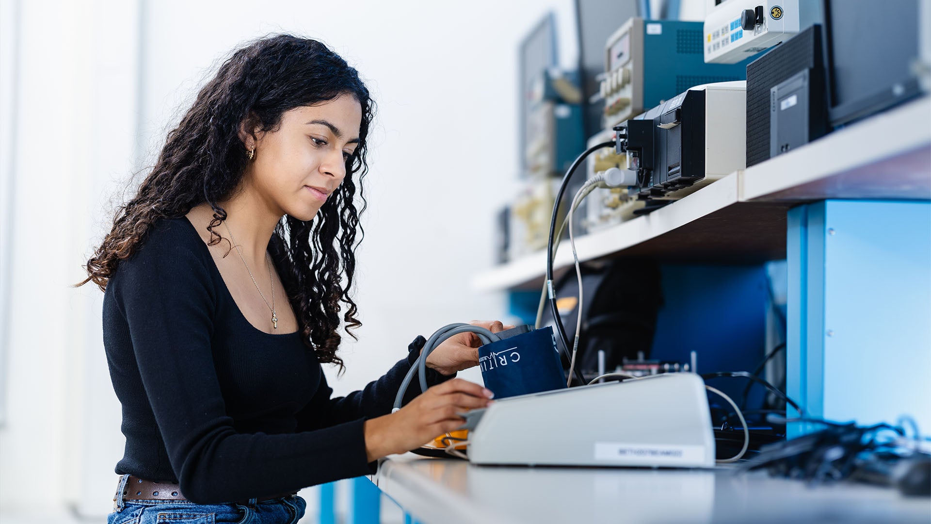 A female biomedical engineering student working at a desk, examining a blood pressure cuff.