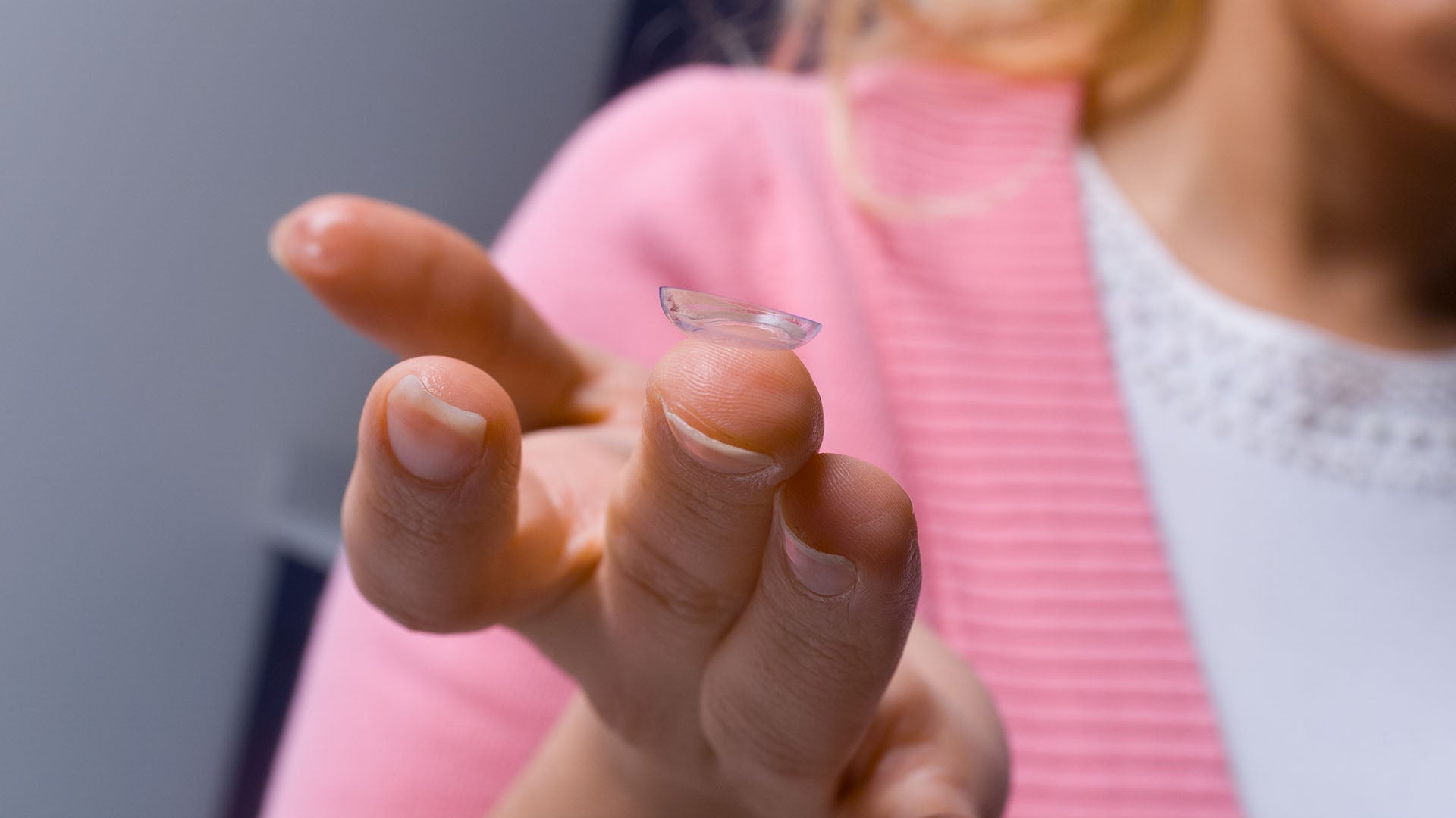 A close-up shot of a woman's finger holding a contact lens.