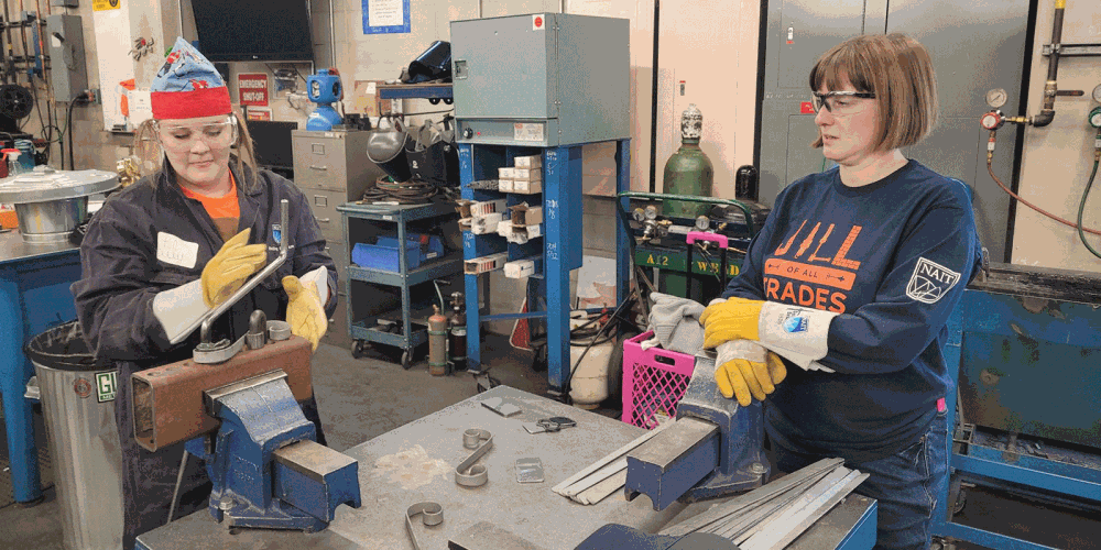 Two women in a workshop wearing safety goggles and globes working with metal