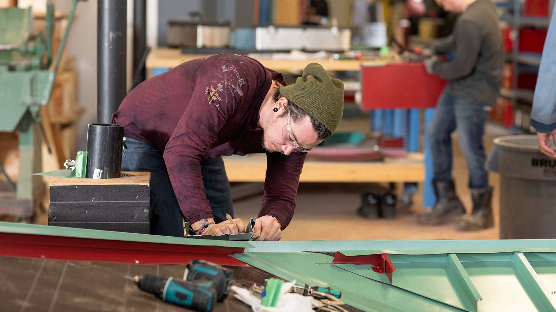 Male roofing student wearing safety glasses working on a tin roof.