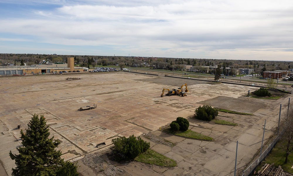 Aerial view of a large cleared construction site with concrete foundations and two excavators in an urban area.