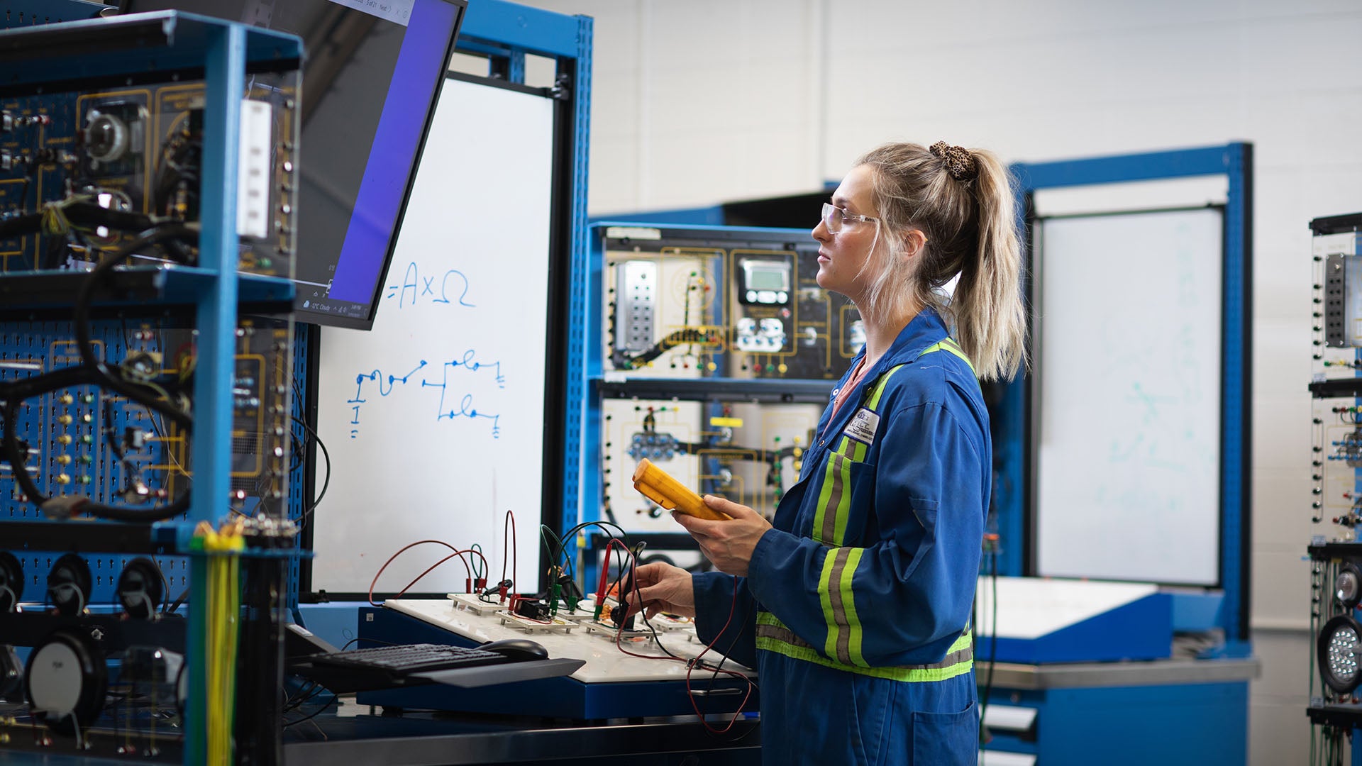 A female Heavy Equipment Technician testing equipment while watching a screen.