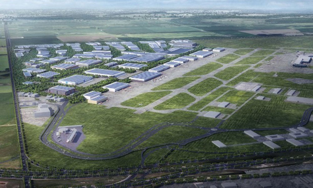Artist rendering of a large airport cargo and logistics hub featuring warehouses, roadways, and industrial facilities spread across a landscaped site beside airfield infrastructure.