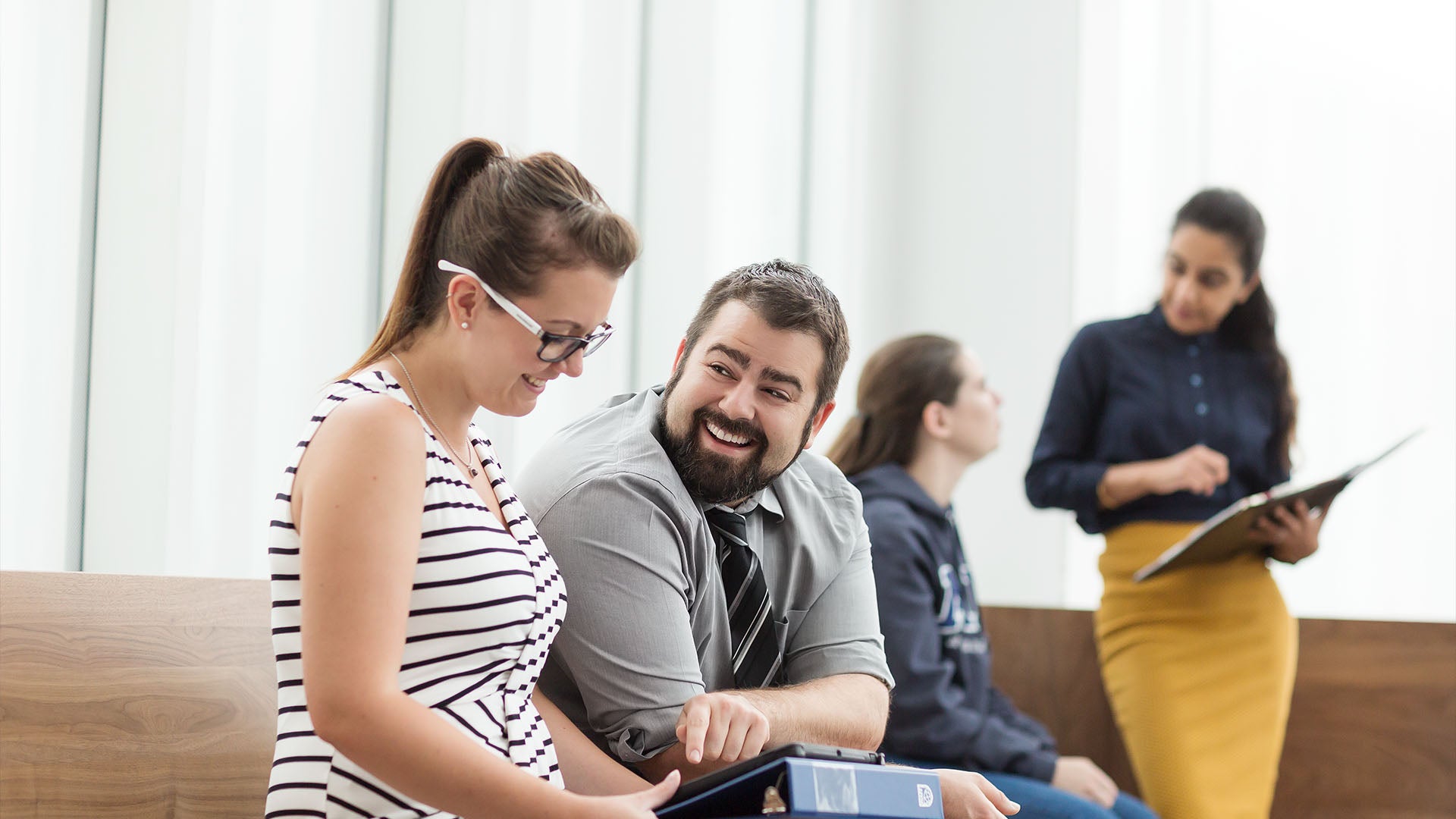 Two NAIT Human Resource Management students look at a tablet while smiling at each other. 