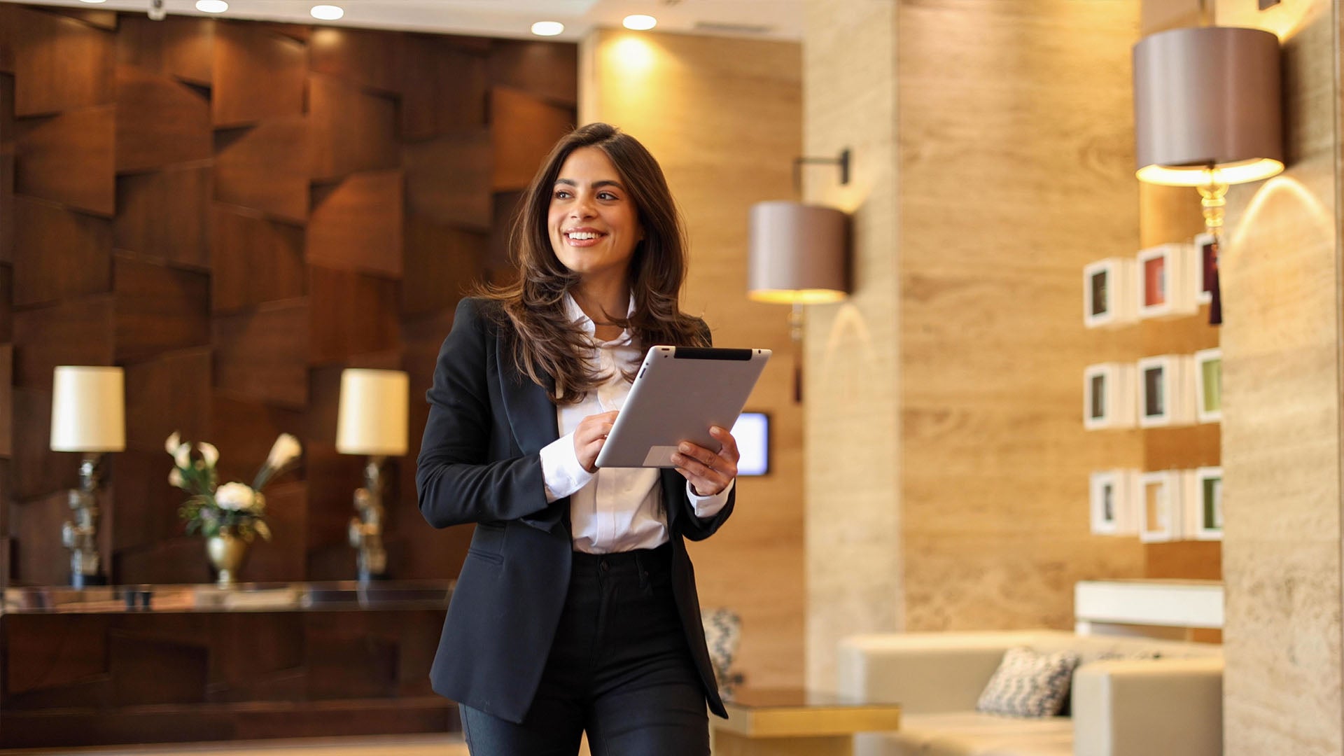 A smiling hotel receptionist assisting a guest at the front desk, with a bowl of apples and a professional atmosphere in the background.