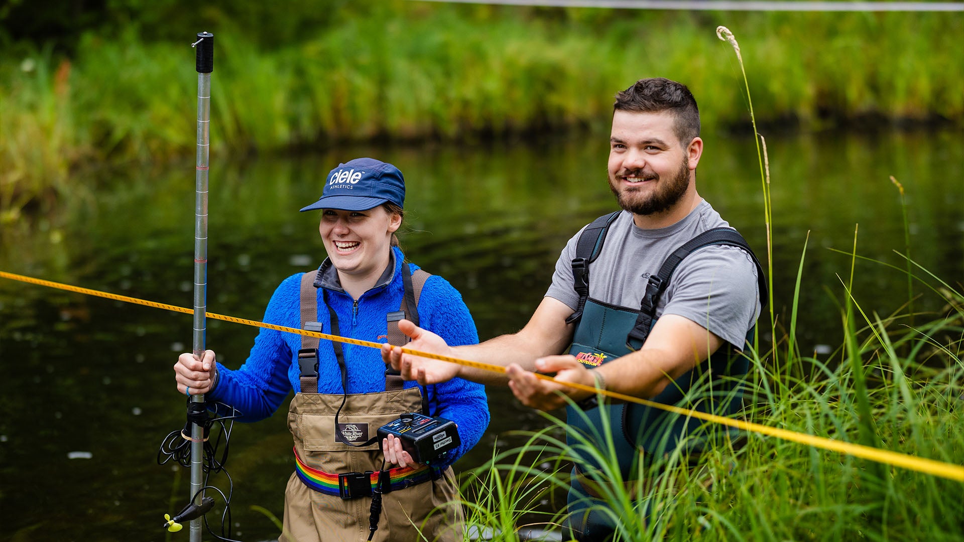 Two conservation biology students standing in water, wearing hip waders, while conducting fieldwork.