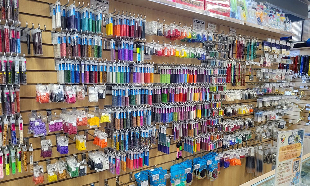 Wall display of colorful beads and jewelry-making supplies organized in rows on pegboard shelves inside a store.