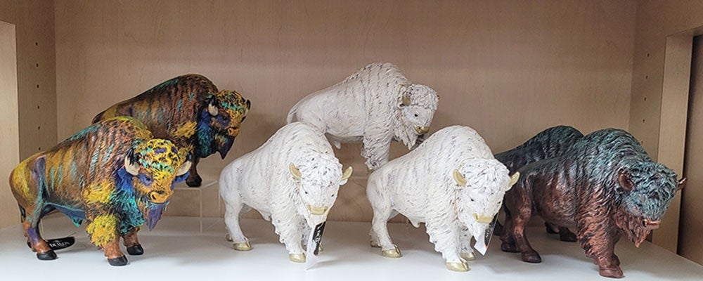 Decorative bison figurines in various colours and finishes displayed on a wooden retail shelf.