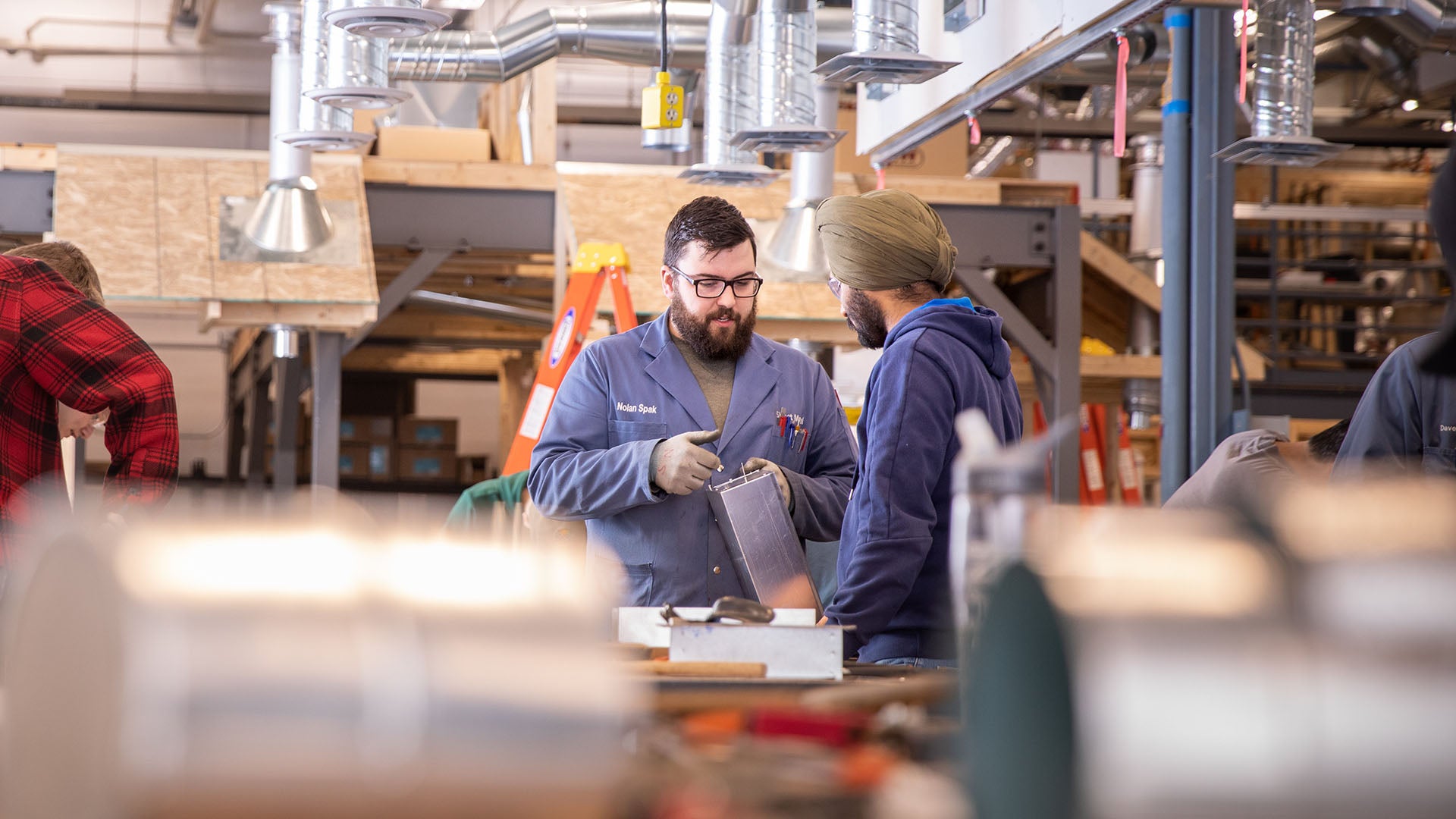 A sheet metal instructor talking to a student in a workshop.