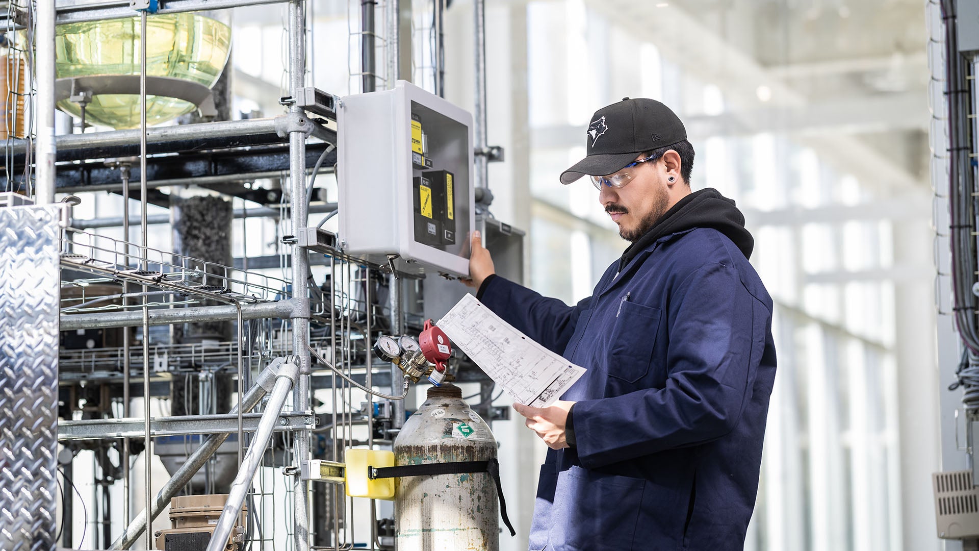 A male instrumentation and control technician reviews schematics while standing in an industrial plant.