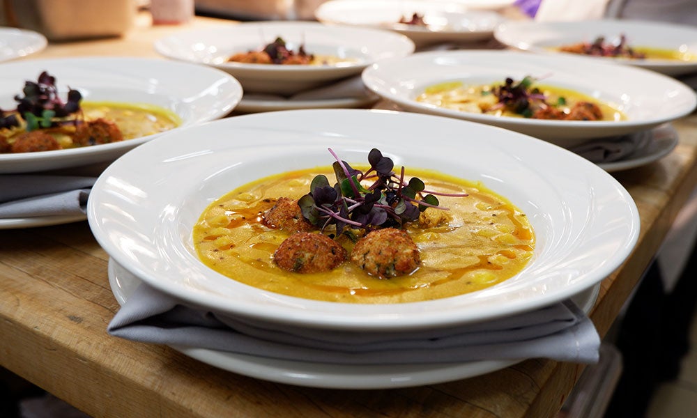 Creamy soup garnished with microgreens and crispy fritters, plated in white bowls on a wooden table.
