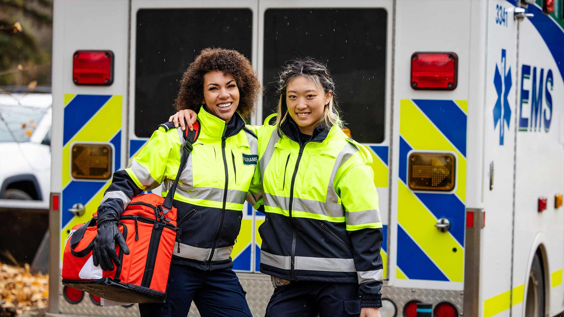 Two women in reflective jackets standing in front of a ambulance.