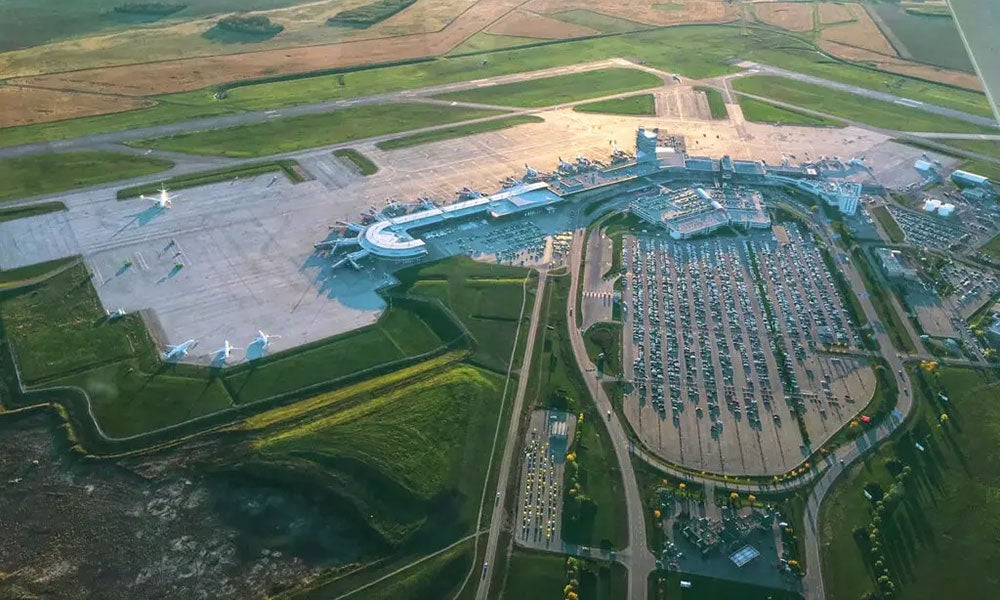 Aerial view of Edmonton International Airport showing terminal buildings, aircraft stands, parking lots, runways, and surrounding farmland.