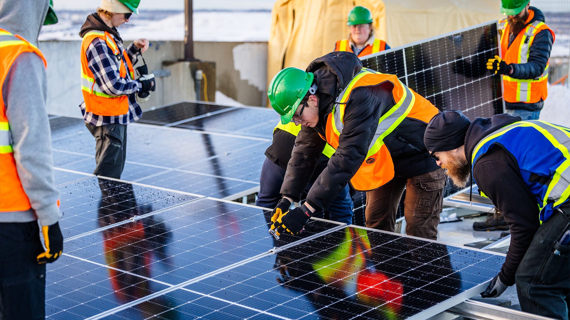 A group of people in orange reflective vests working on solar panels.