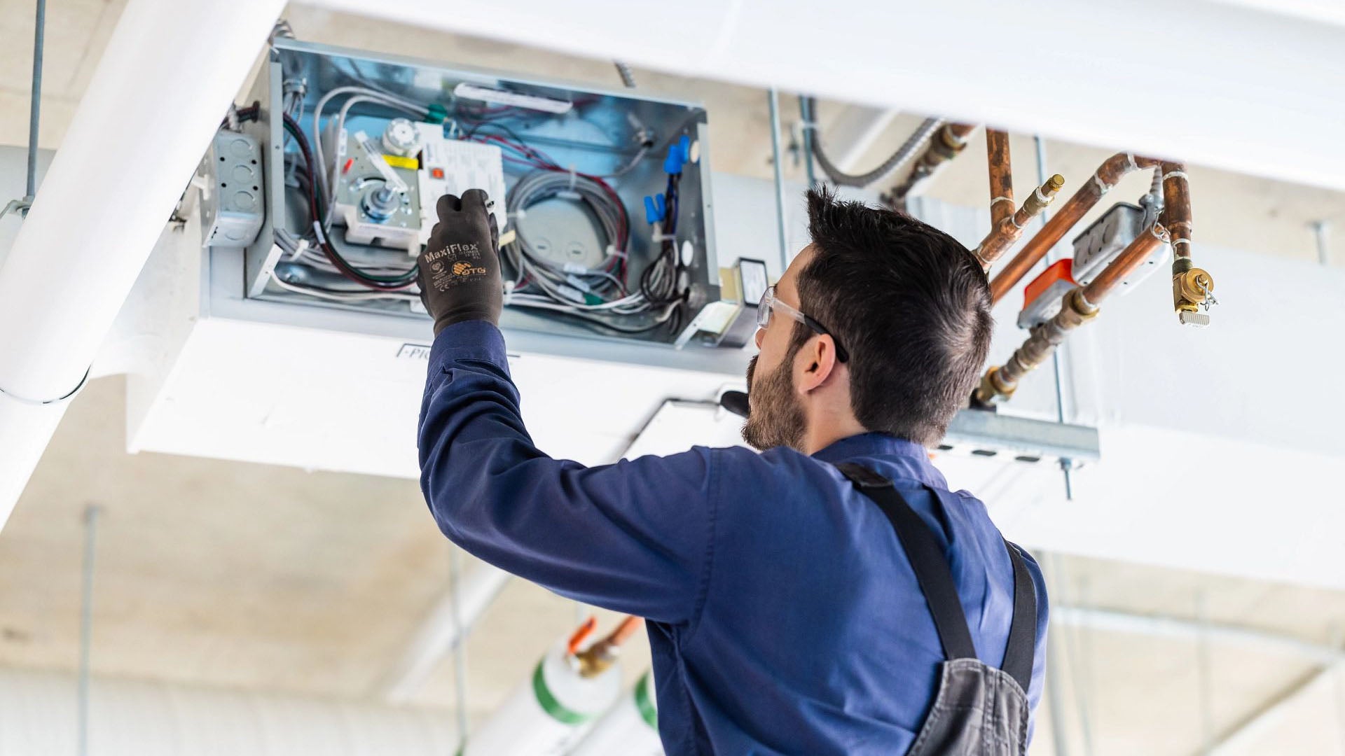 A man examining and adjusting electrical components inside a ceiling-mounted unit.