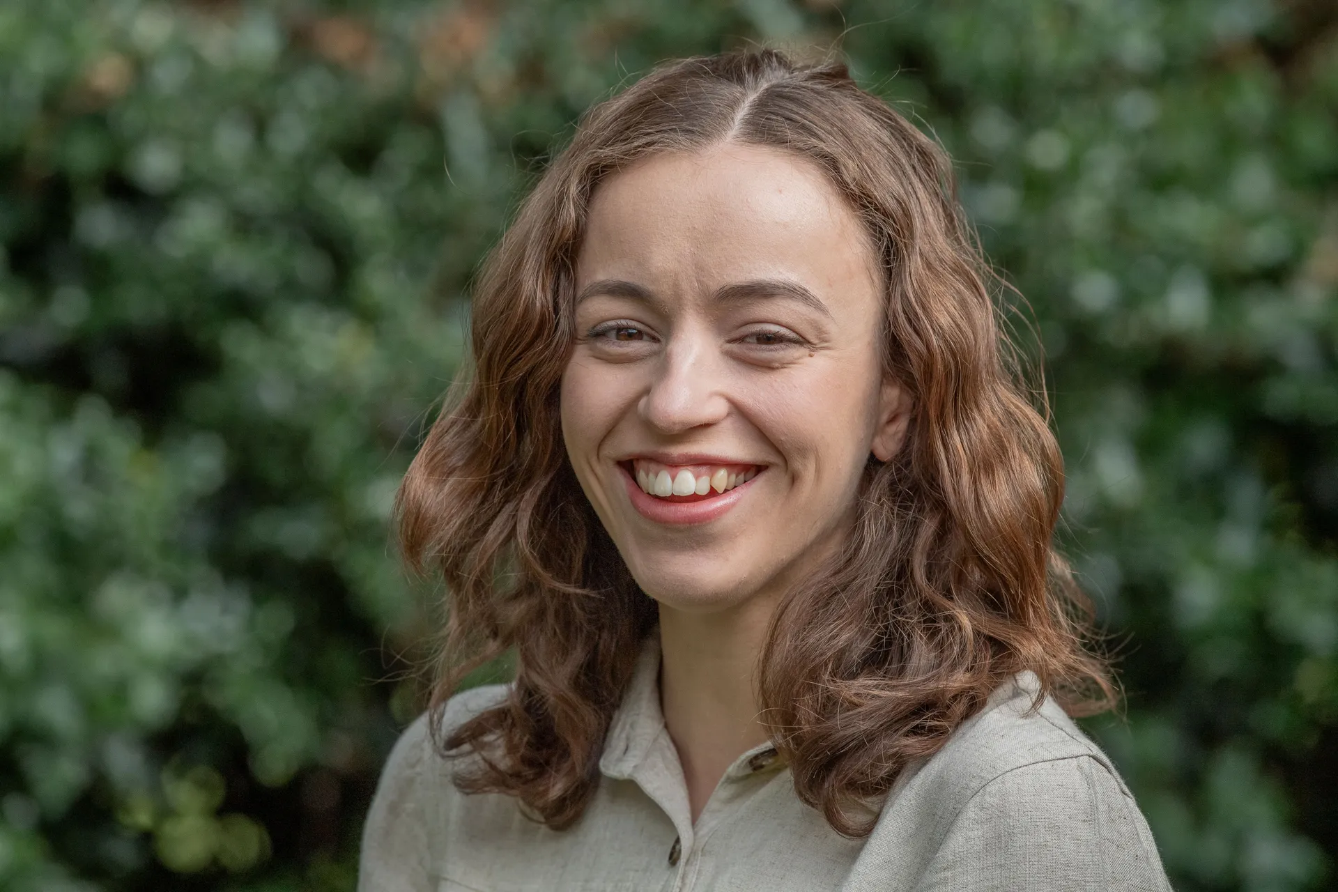 headshot style portrait of a young woman standing in front of a leafy bush