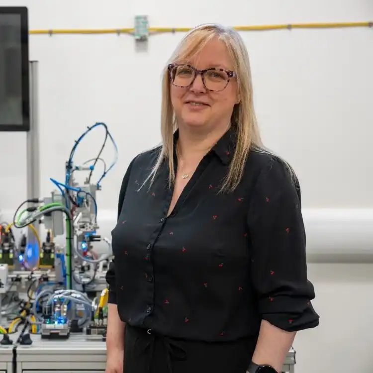 A blonde woman wearing glasses and a black top, in a workshop
